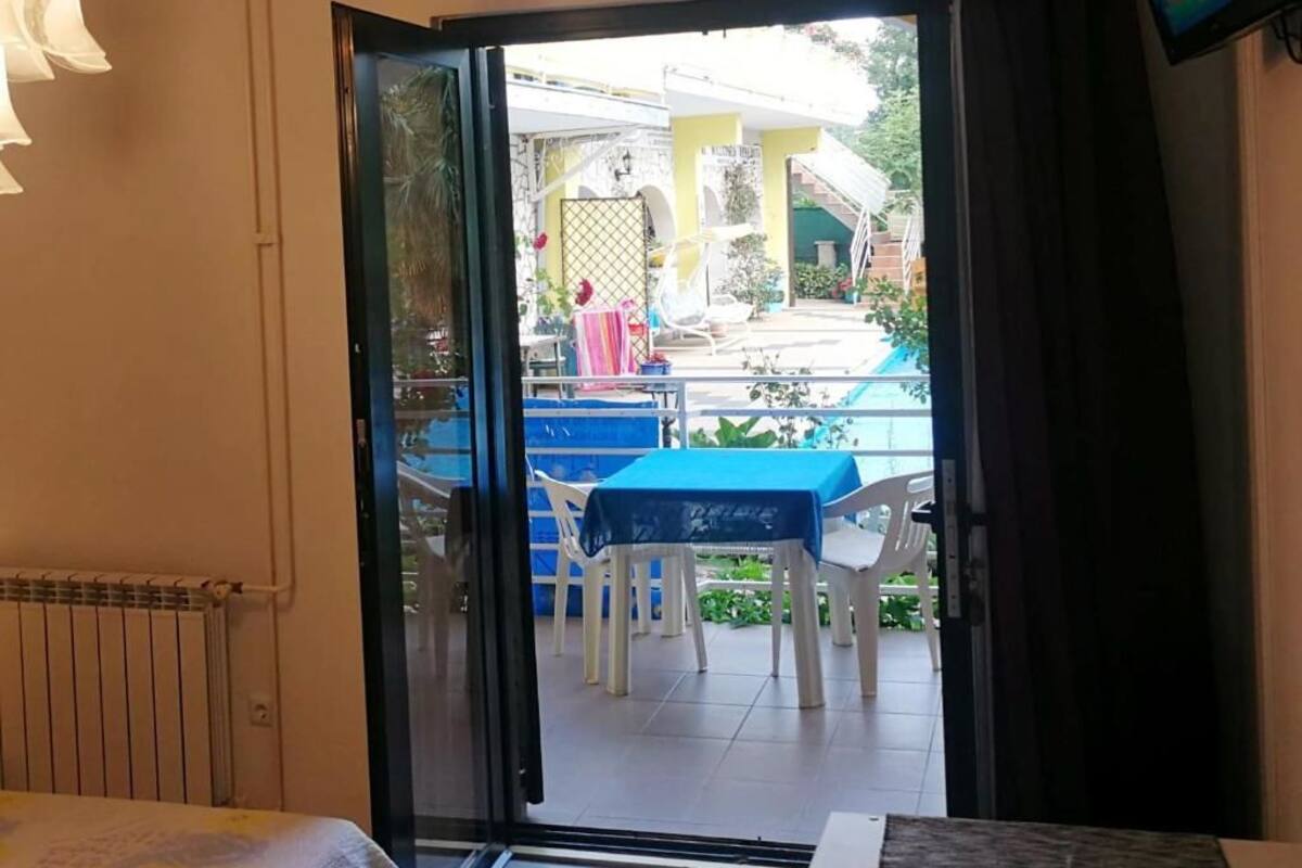 A room with a bed, a sliding glass door leading to an outdoor patio with a pool, chairs, and a table.