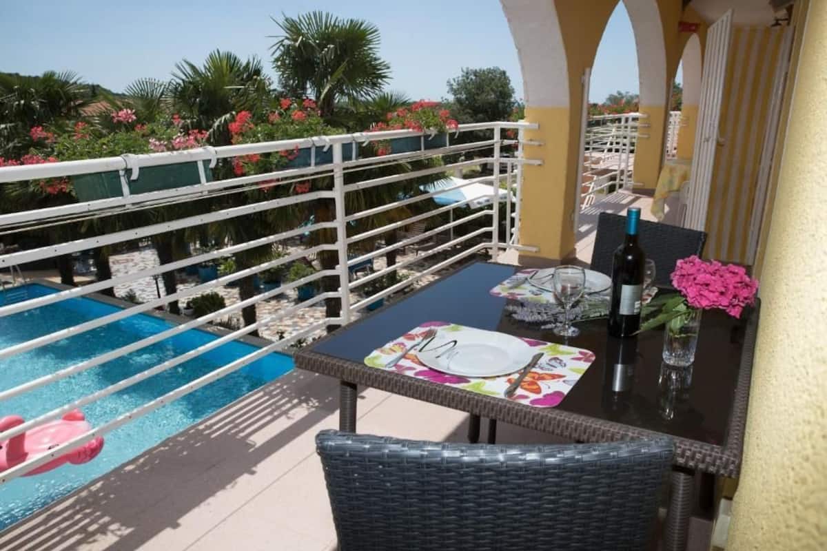 An outdoor dining area with a table set for two, overlooking a pool and a landscaped garden.