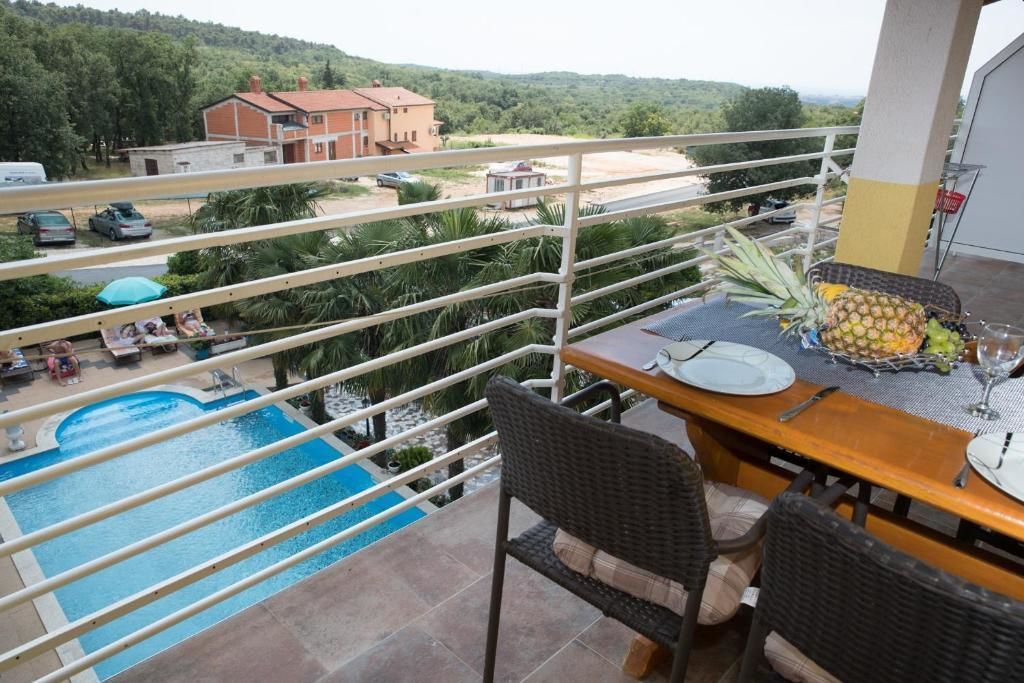 A balcony with a view of a swimming pool, dining table with chairs, and a tropical setting.
