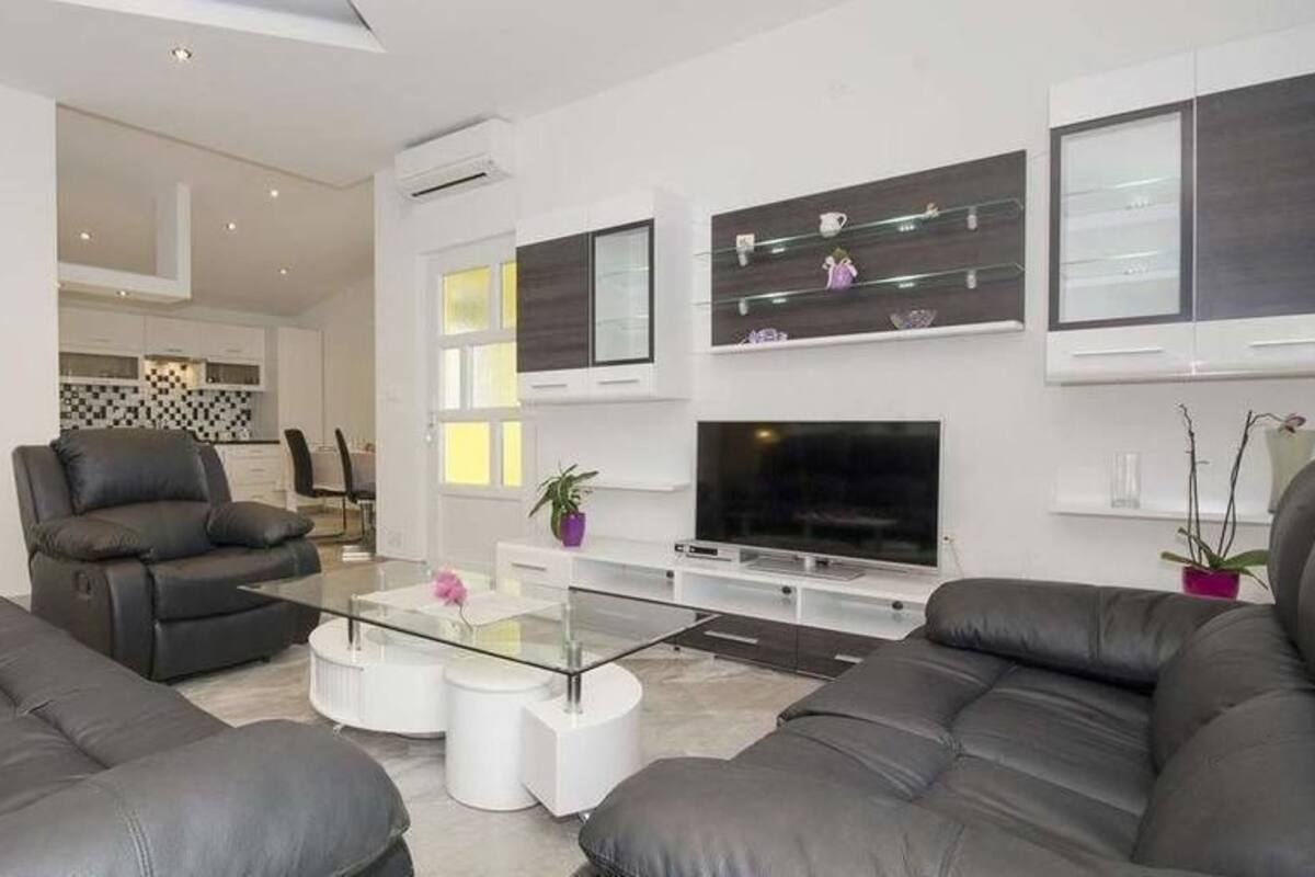 A modern living room with leather sofas, a glass coffee table, a flat-screen TV, and minimalist decor.