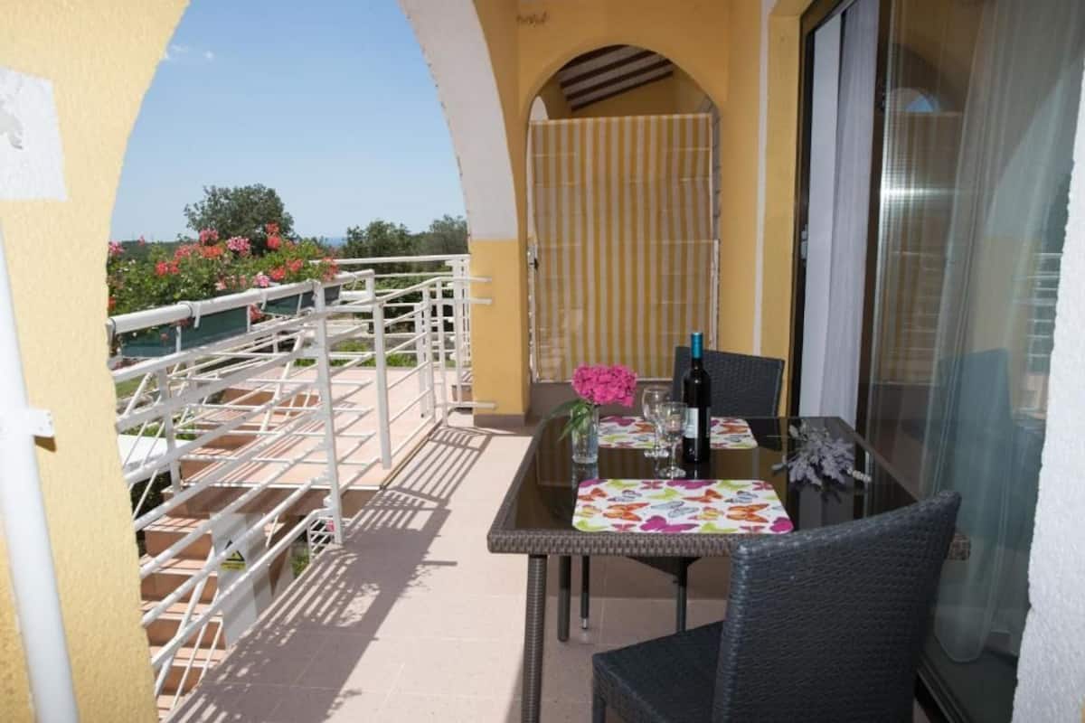 A balcony with a table set for two, a chair, and a glass door leading to a terrace.