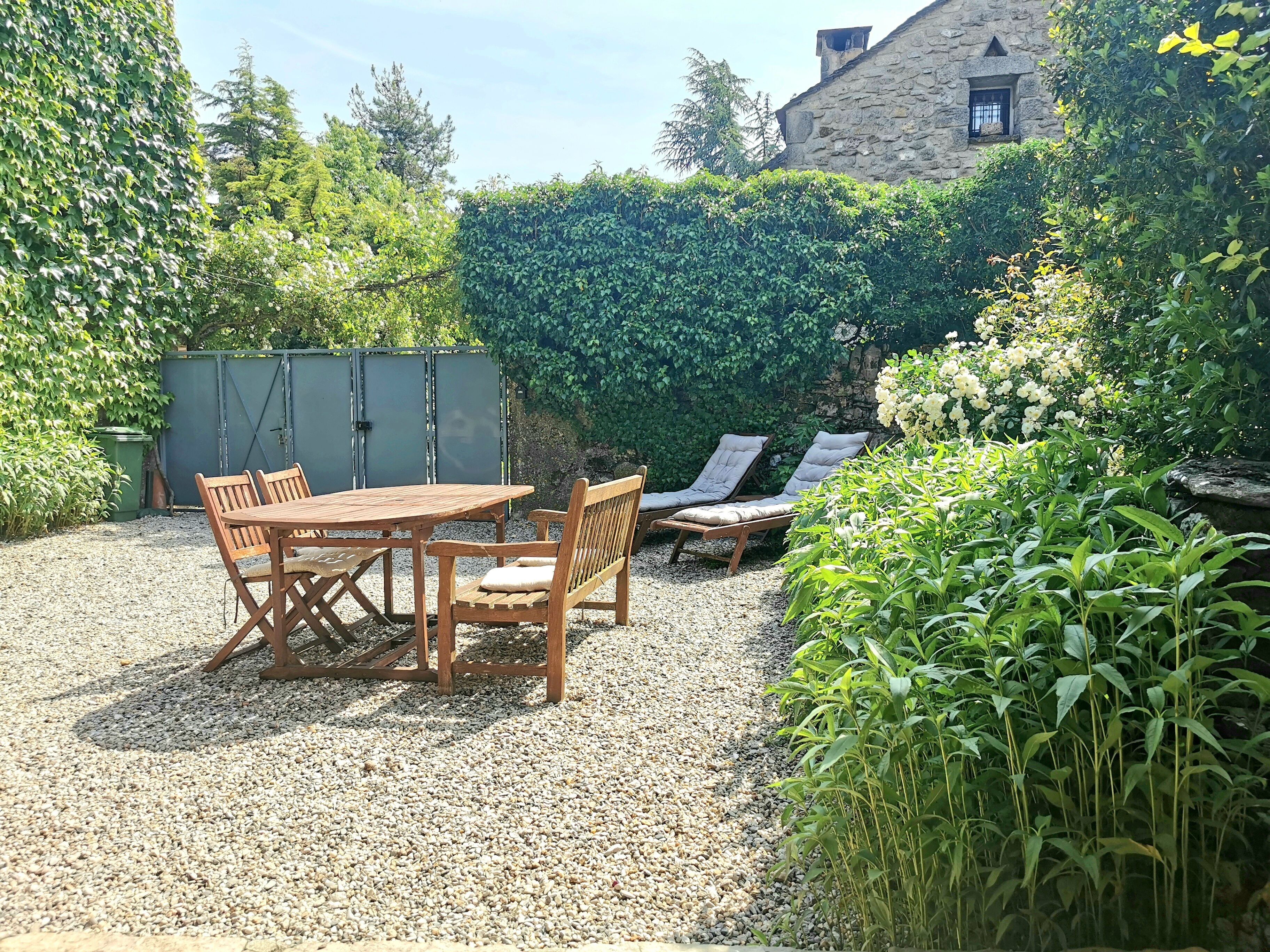 Een terras met een houten tafel en stoelen, omringd door grind en beplanting.