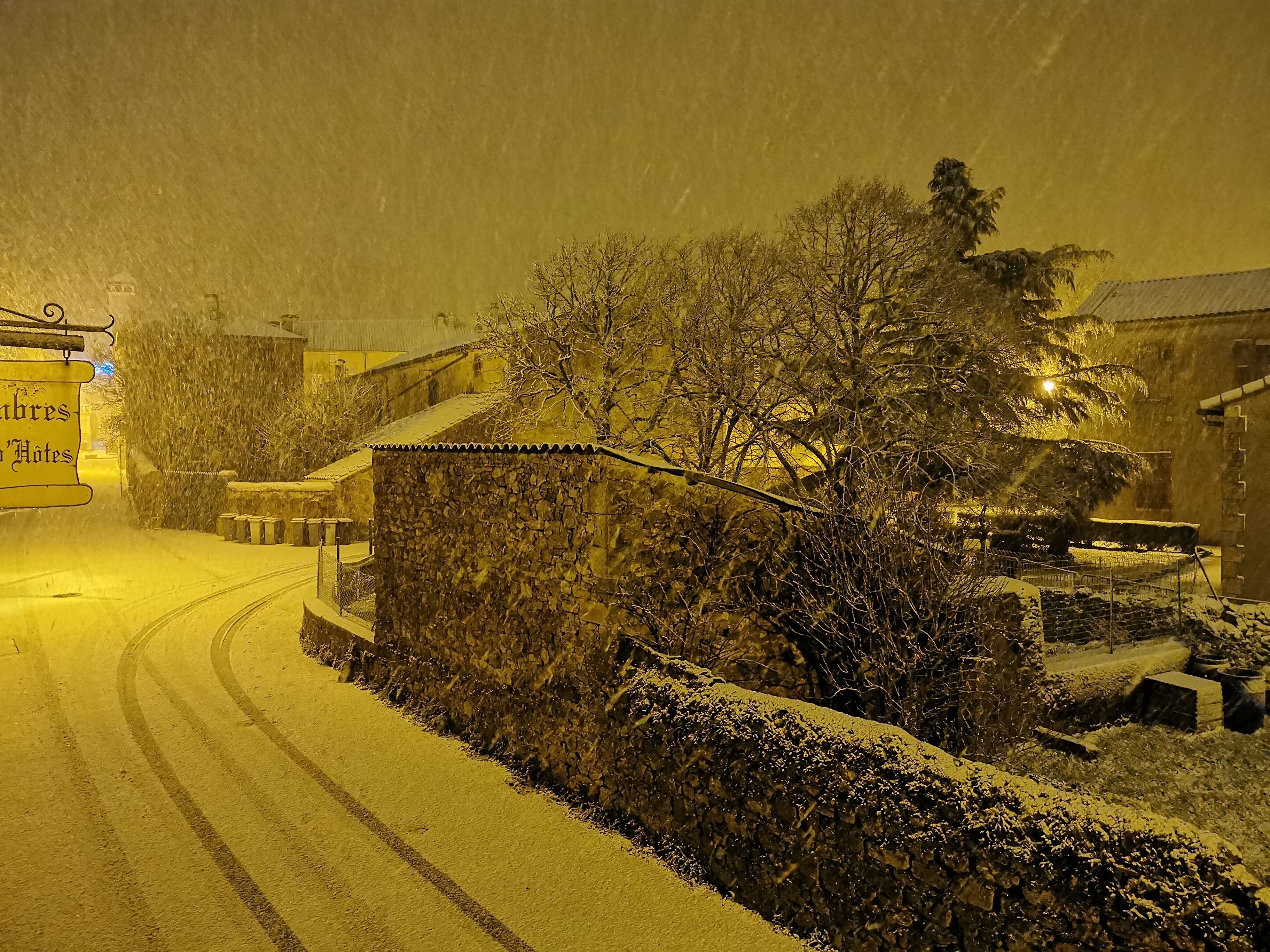 Eine verschneite Straße mit einer Steinmauer und einem Gebäude, an dem das Schild "Hotes" steht.