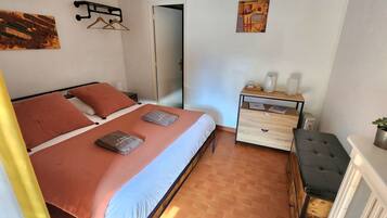 Un dormitorio con cama, mesita de noche, silla y puerta.