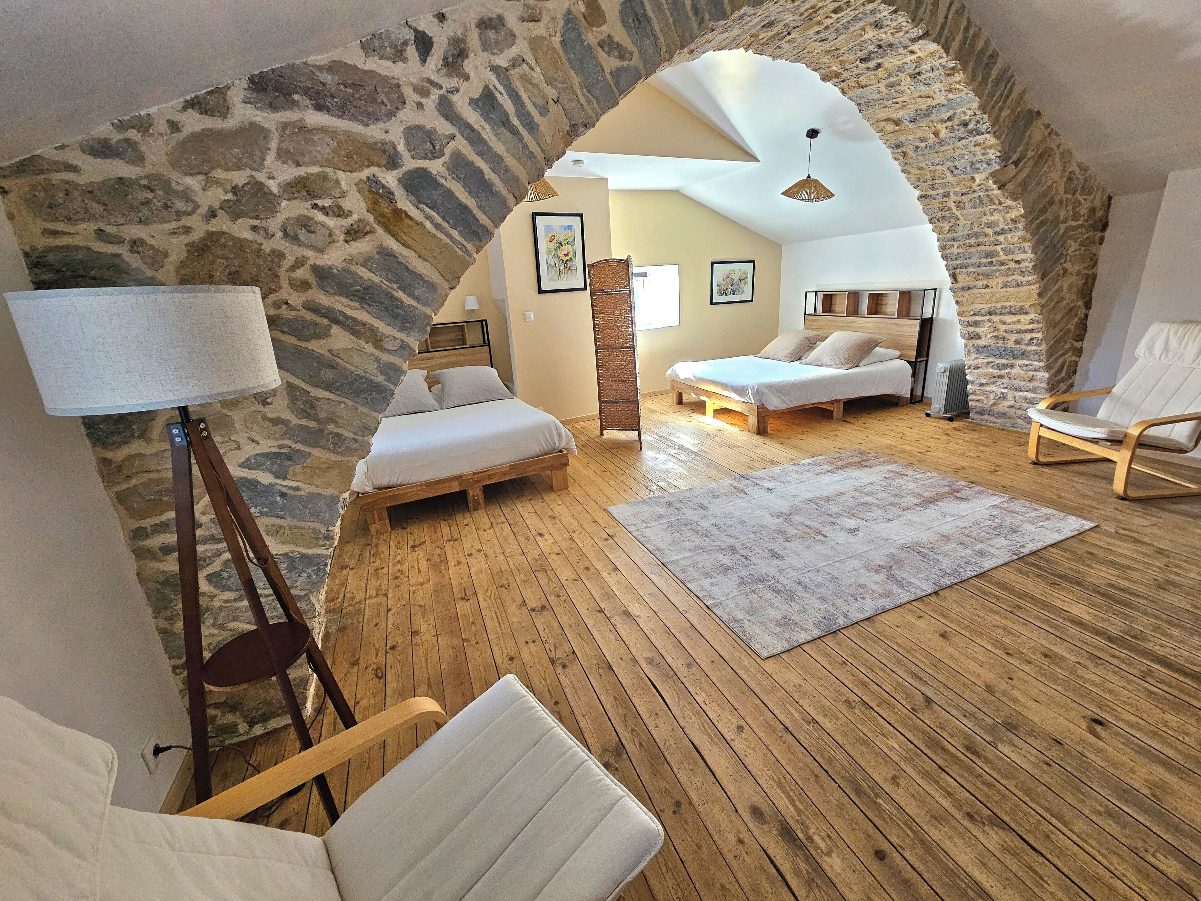 Une chambre confortable située dans les combles, avec un mur en pierre, un plancher en bois, un lit, une chaise, une lampe et un canapé.