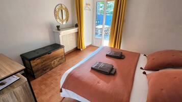 A bedroom with a bed, a chest of drawers, a bedside table, a mirror, and a view of the outside.