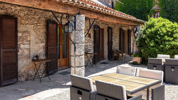Un bâtiment en pierre avec un toit en tuiles, un espace extérieur aménagé avec des meubles en osier et une petite table sur laquelle est posée une plante en pot.