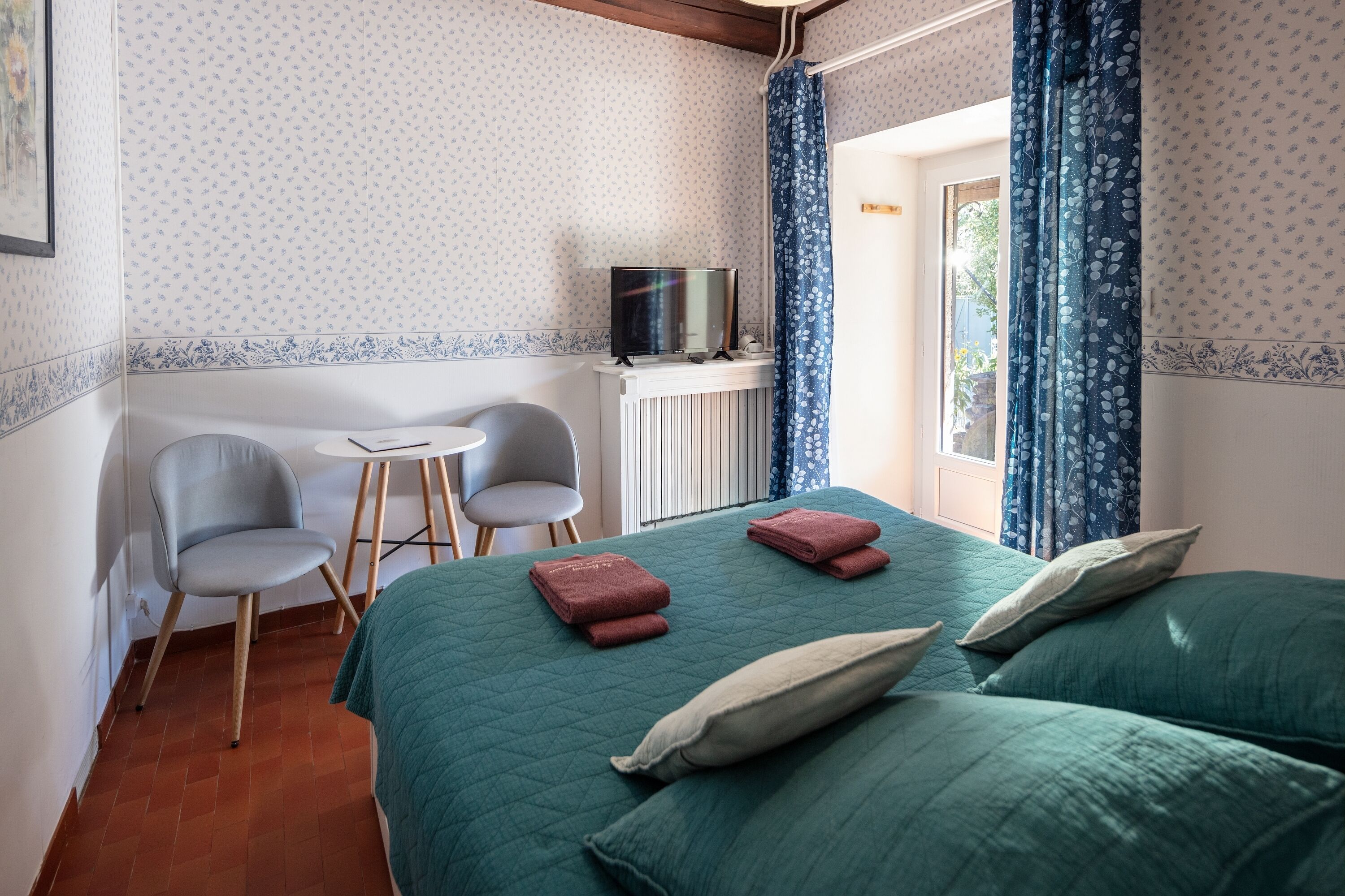 A room with a bed, two chairs, a small table, and a television.