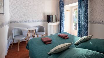A room with a bed, two chairs, a small table, and a television.