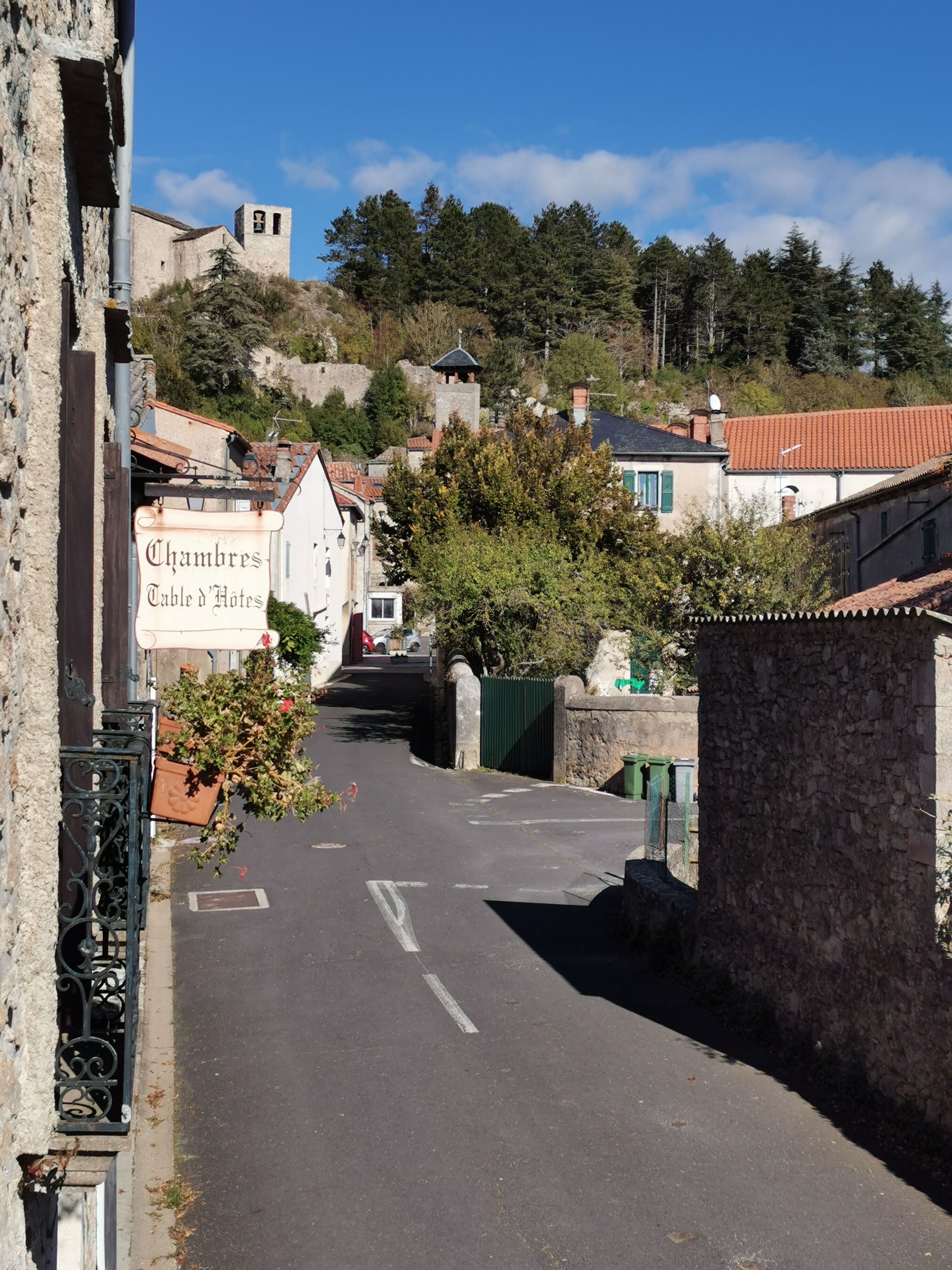 Una calle estrecha flanqueada por edificios, un letrero que dice 'Chambres Table d'Hôtes' y una pared de piedra a la derecha.