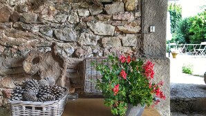 Un mur de pierres, un panier en osier et un pot de fleurs rouges posés sur une table en bois.