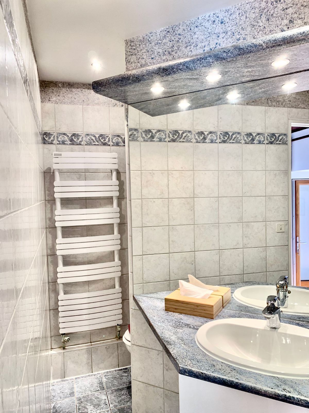 Een badkamer met een witte handdoekhouder, twee wasbakken en een spiegel.