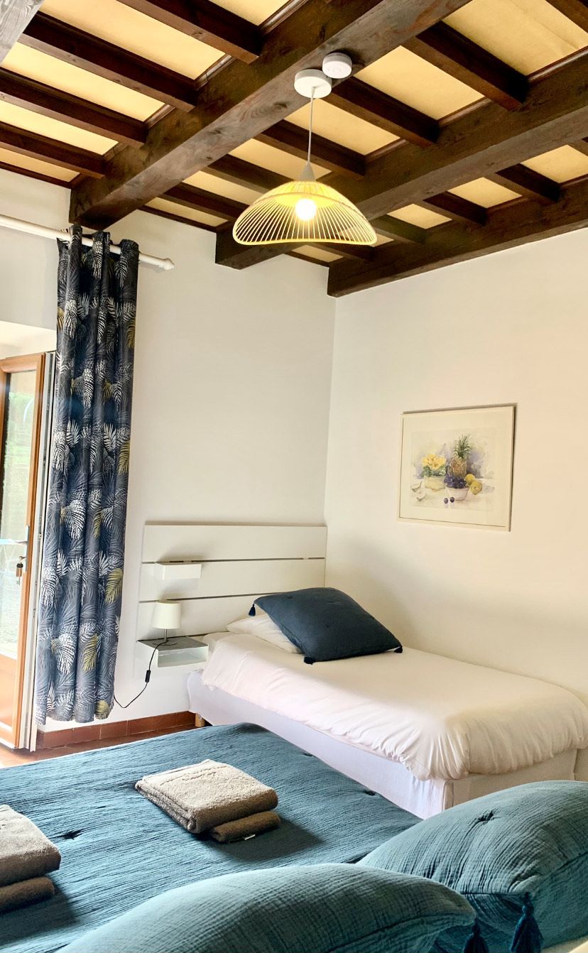 A bedroom with a bed, a bedside table, a lamp, a painting, and a window with curtains.