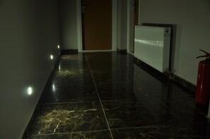 A corridor with a shiny black marble floor, a white radiator, and a red fire extinguisher. - Osmanli Omtel Otel (Boyabat)