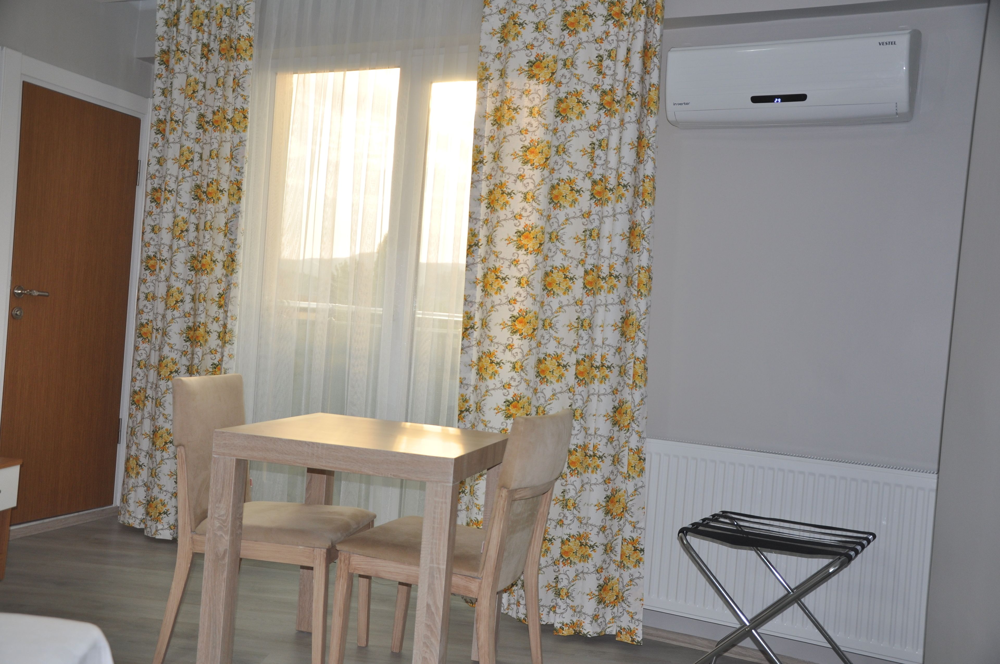 Una habitación con una mesa y sillas de madera, un radiador y una ventana con cortinas florales.