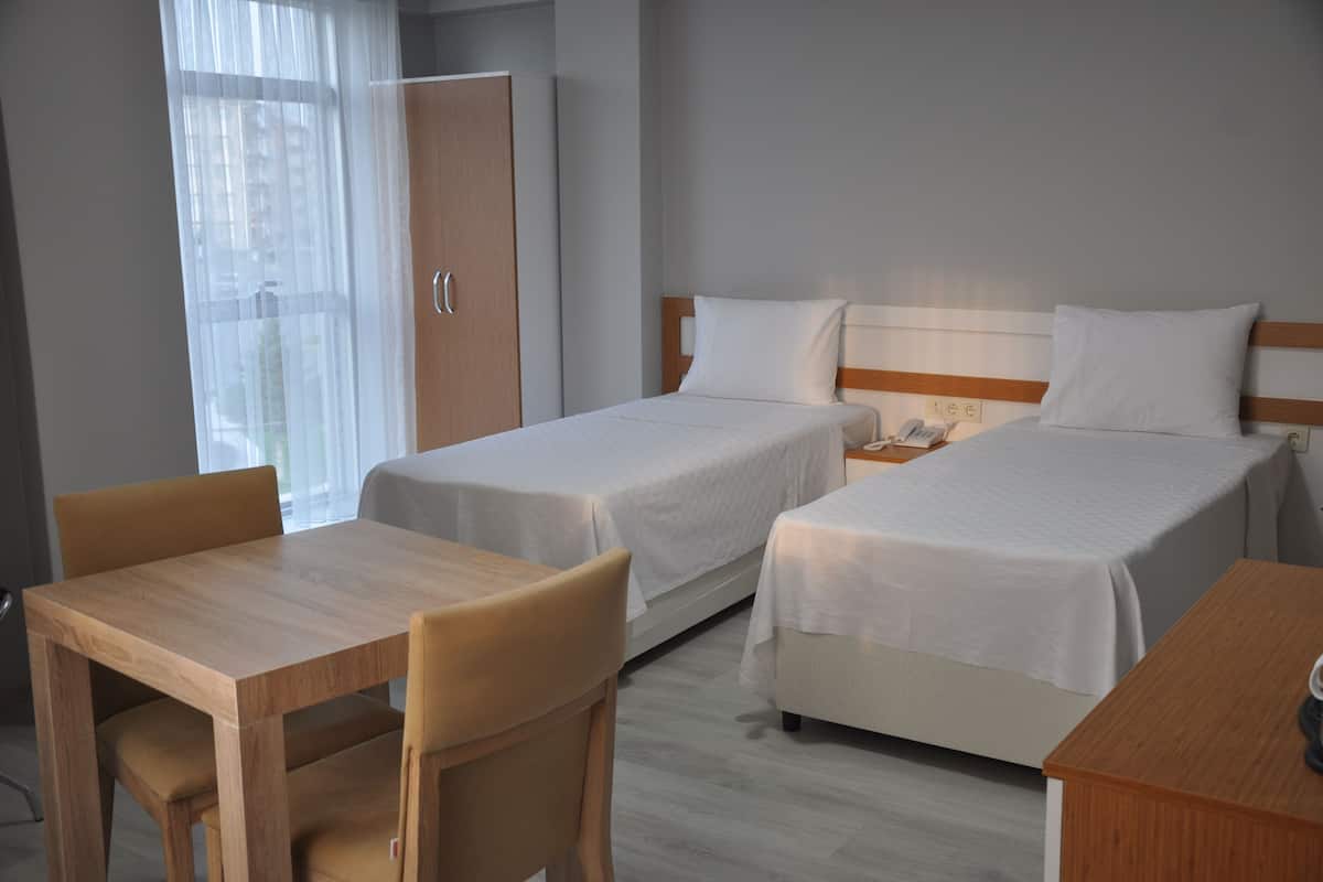 A hotel room with two single beds, a wooden desk, a chair, a wardrobe, and a window with sheer curtains.