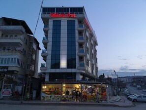 A hotel with a modern facade, multiple balconies, and a ground-level shop with colorful fruit displays.