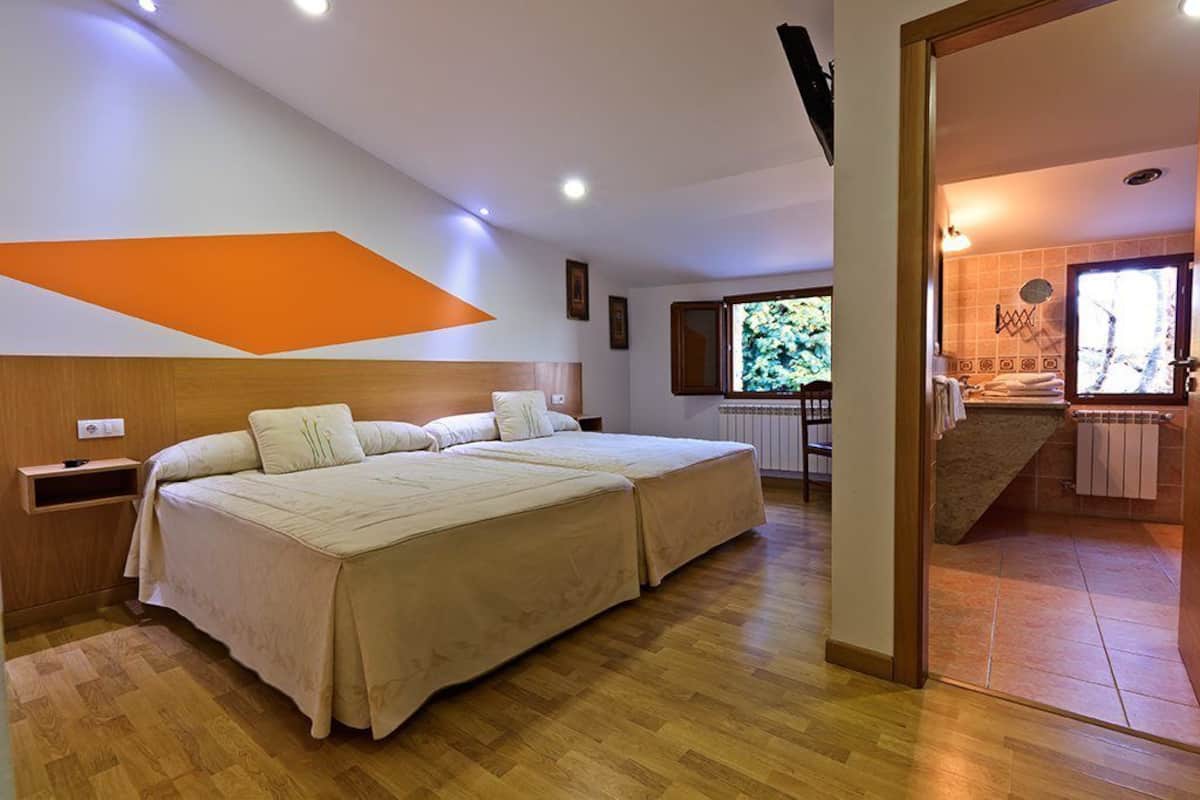 A bedroom with two beds, a wooden headboard, a TV, and a bathroom visible through an open door.