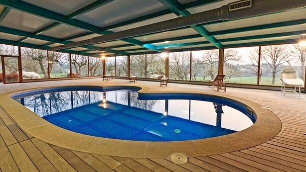 Une piscine couverte dotée d’une terrasse en bois, de bancs et offrant une vue sur le paysage environnant.