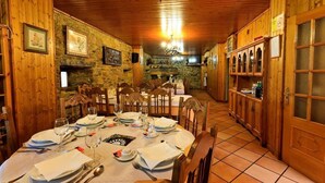 Une salle à manger aux murs lambrés, avec un mur en pierre, un lustre et un téléviseur.