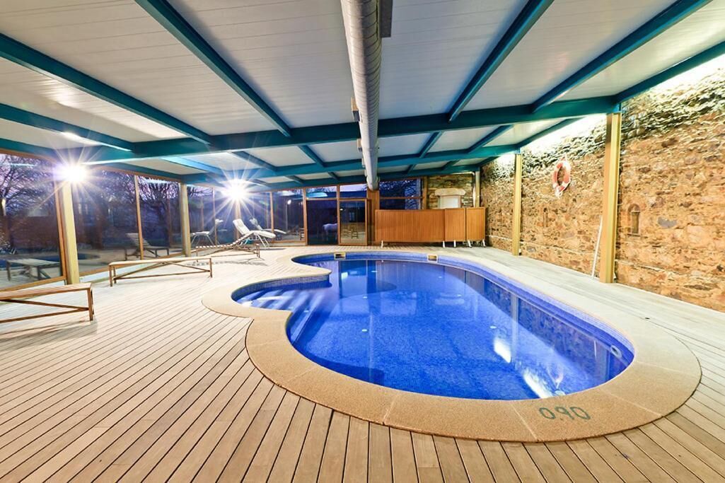 A swimming pool with a wooden deck, stone walls, and a covered roof structure.