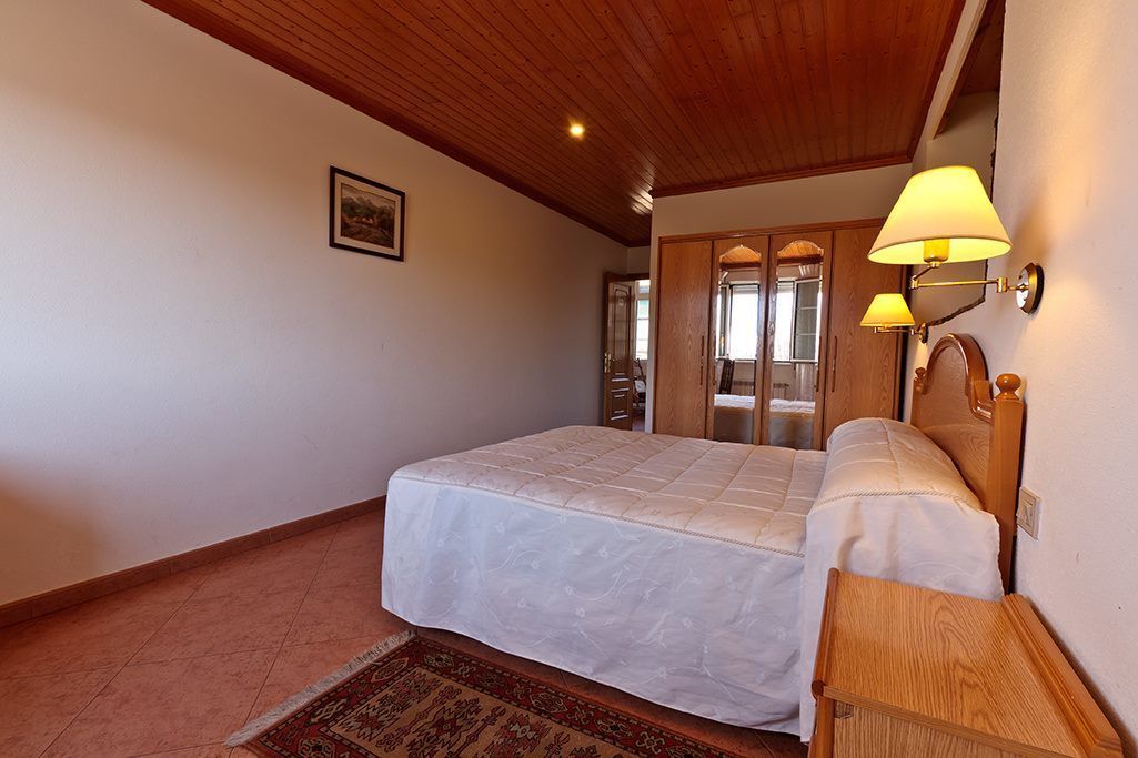 Un dormitorio con una cama grande, techo de madera y dos lámparas de pared.