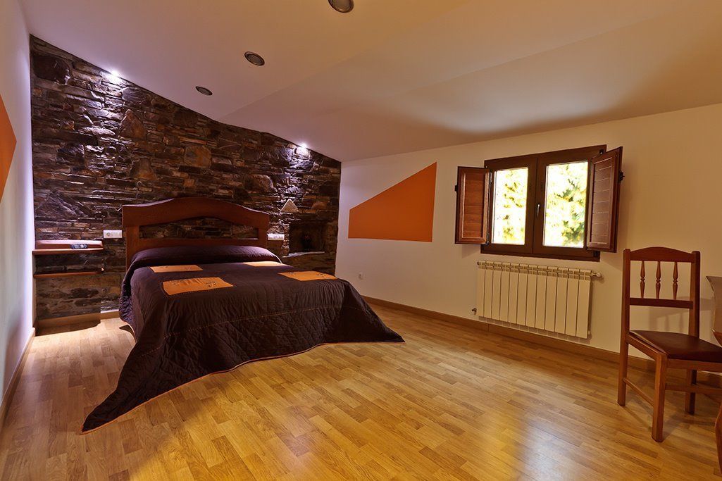 Ein Schlafzimmer mit Steinsturz, Bett mit Kopfteil, Fenster mit Rollläden, Heizkörper und einem Holzstuhl.