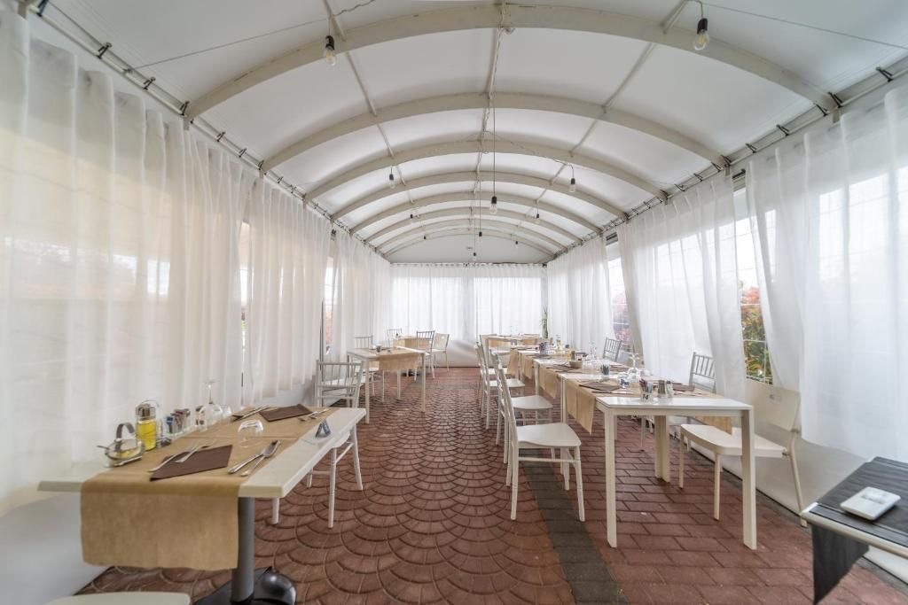 Een lange, overdekte eetruimte met tafels en stoelen, een patroon vloer en een hoog plafond met zichtbare balken.