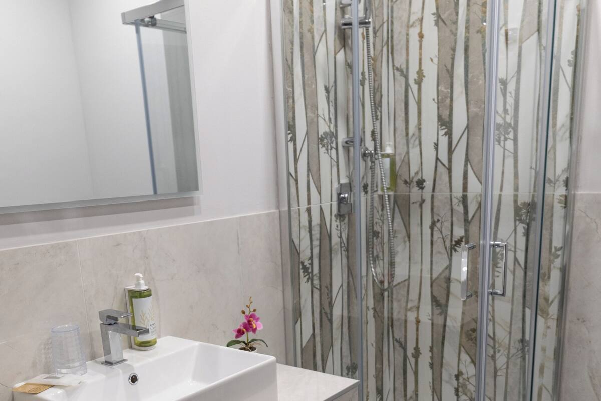 A bathroom with a white sink, a mirror, a glass shower enclosure, and a marble floor.