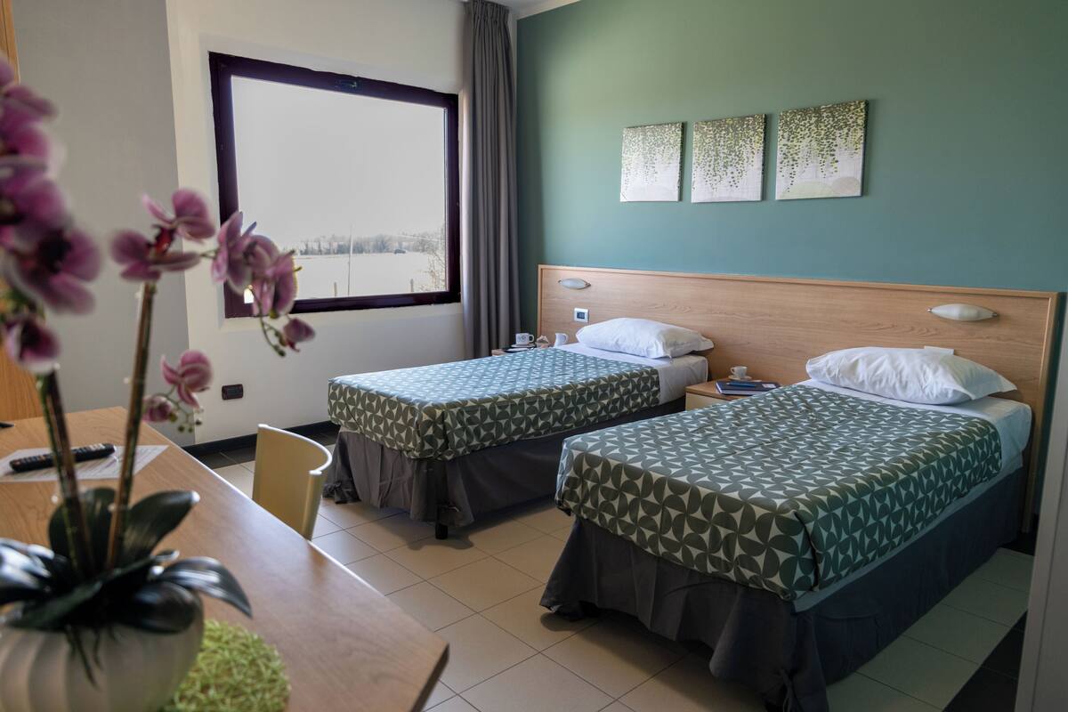 A hotel room with two single beds, a wooden headboard, a large window, and a view of a snowy landscape.