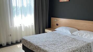 Ein Hotelzimmer mit Bett, Nachttisch, Stuhl und einem Fenster mit Vorhängen.