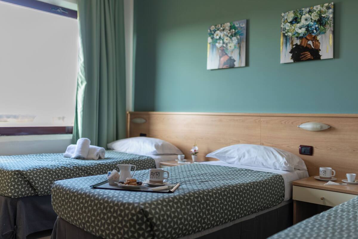 A hotel room with two beds, a wooden headboard, a nightstand with a lamp, and artwork on the wall.