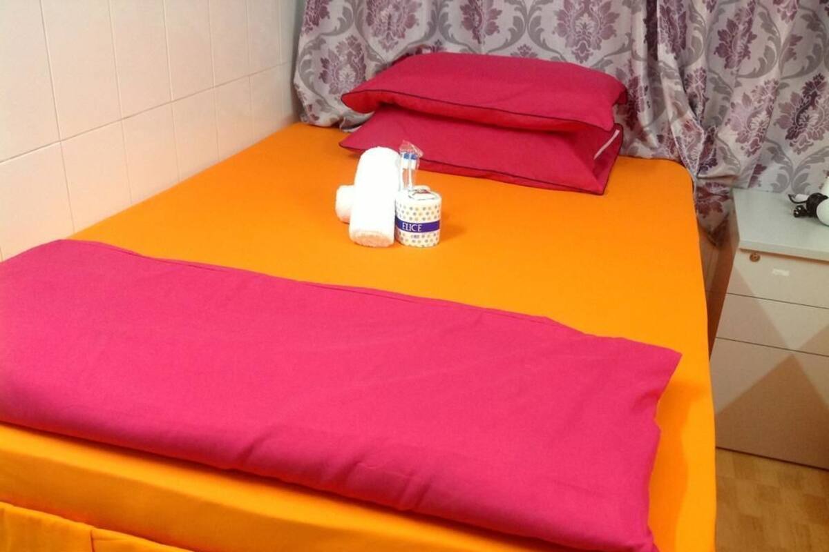 A neatly made bed with bright orange bedding and a pink pillow. There are two bottles and a small container on the bed.