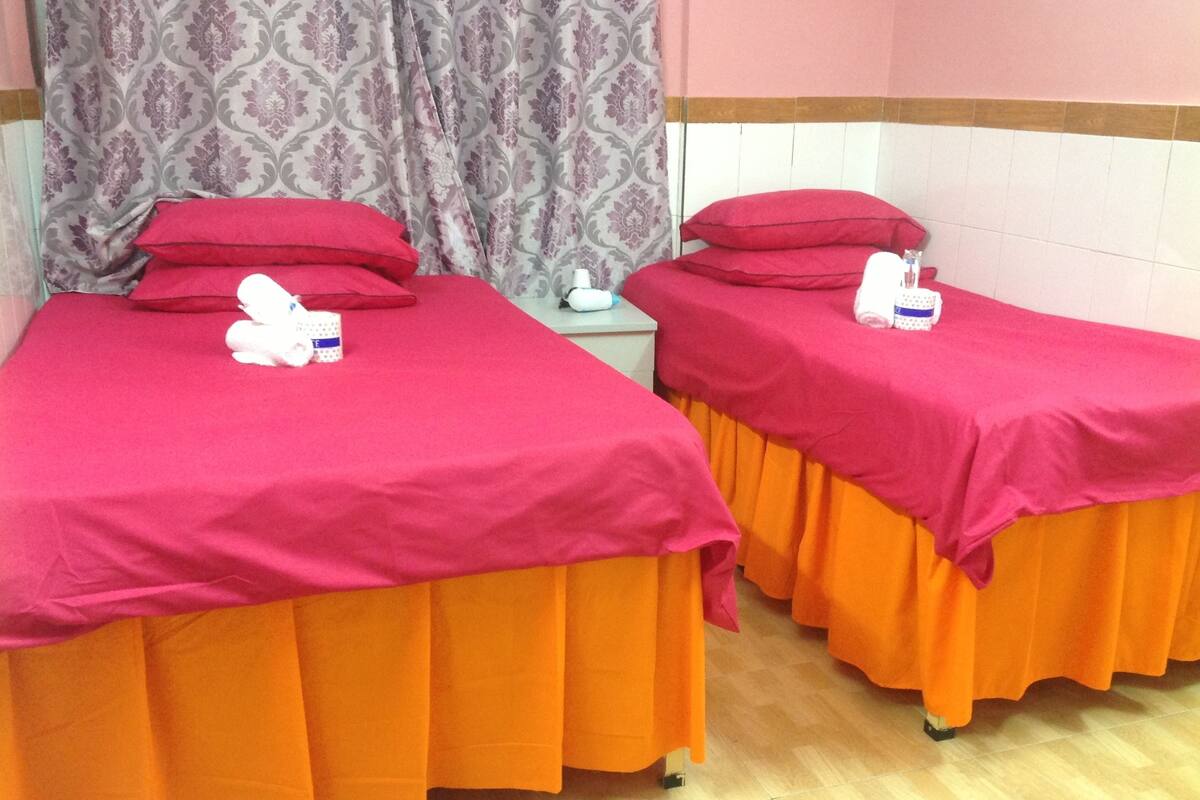 Two single beds with red and orange bedding, a white pillow, and a white stuffed toy on each bed.