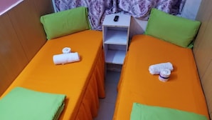 A twin room with two beds, each with an orange bedspread and green pillows. There is a small white nightstand with a remote control on it. - Head Sun Guest House (Kowloon)