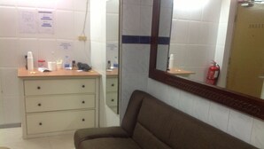 A bathroom with a wooden vanity, a mirror, a brown sofa, and a fire extinguisher. - Head Sun Guest House (Kowloon)