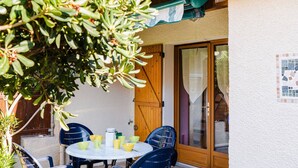 A patio with a round table and chairs, a wooden door, and a tiled wall. - Cozy Villa Studio with Mezzanine, Terrace, and Parking near Narbonne-Plage (Narbonne-Narbonne Plage-Narbonne Plage)