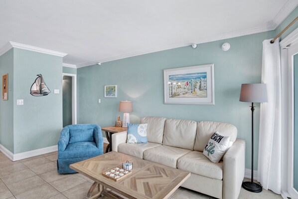 Un salón con un sillón azul, sofá color beige y una mesita de centro con adornos.
