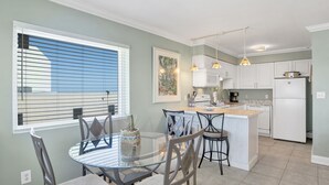Een moderne keuken met een glazen eettafel, witte keukenkastjes en hanglampen.