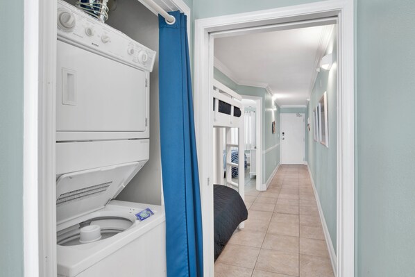 Un área de lavandería con lavadora y secadora, una cortina azul y un pasillo que lleva a un dormitorio.