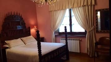 A bedroom with a four-poster bed, a chandelier, a radiator, and a window with curtains.