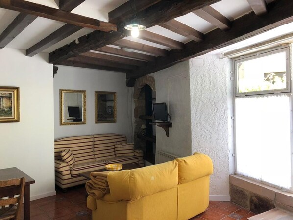 Una sala de estar con un sofá amarillo, un sofá a rayas, un televisor en una estantería y un ventanal con vistas.