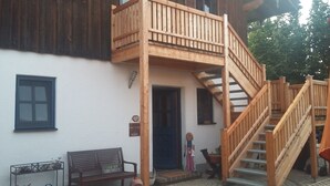 A wooden staircase leading to a balcony, a bench, and a door with a sign. - Ferienwohnung im 1.Stock mit überdachter Terrasse und See- und Bergblick (Chieming)