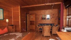 A wooden cabin interior with a bed, a table, wicker chairs, and a television. - Ferienwohnung im 1.Stock mit überdachter Terrasse und See- und Bergblick (Chieming)