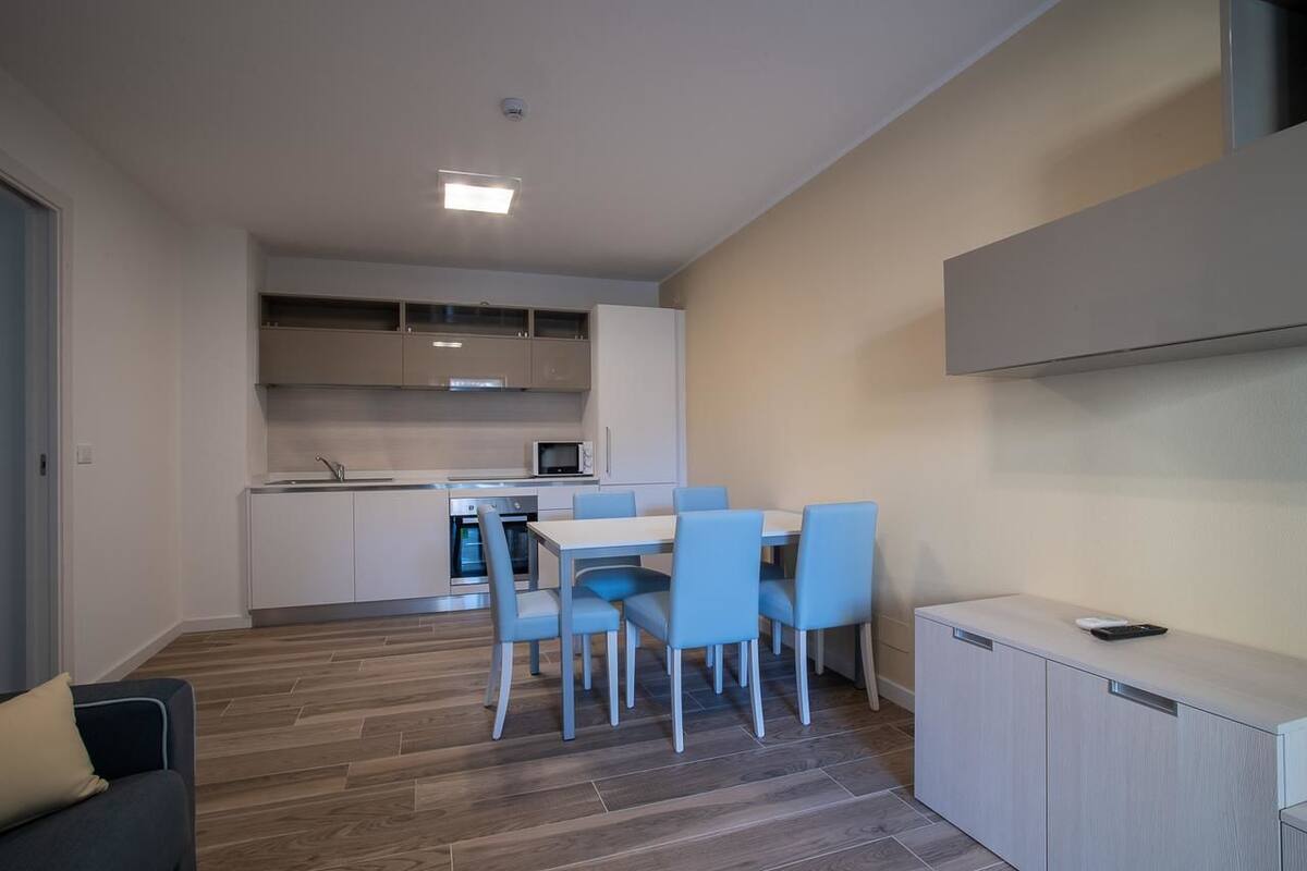 A modern kitchen with white cabinets, a dining area with blue chairs, and a built-in microwave.