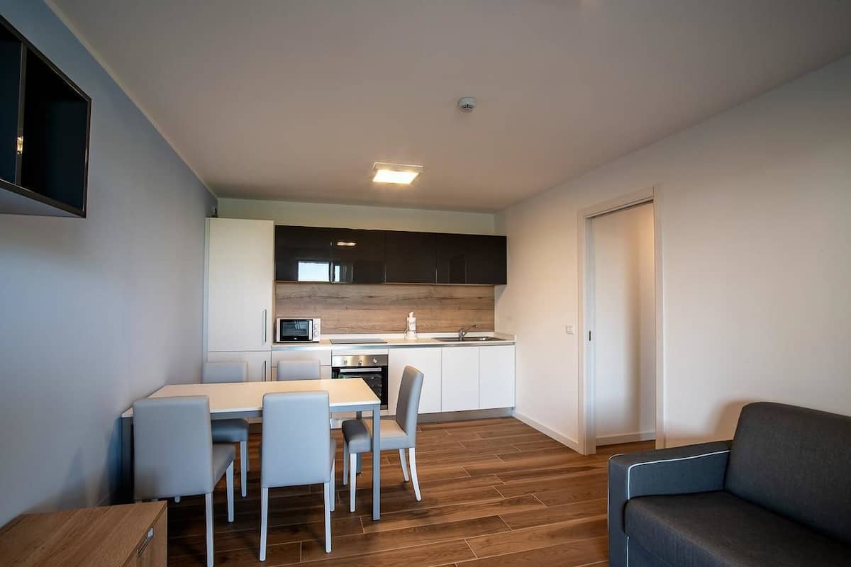 A modern kitchen with white cabinets, a microwave, and a sink. There is a dining table with four chairs.
