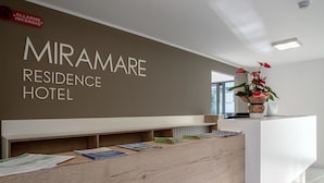 A reception desk at Miramare Residence Hotel with a sign, a plant, and some brochures. - Aparthotel Miramare (Grado)
