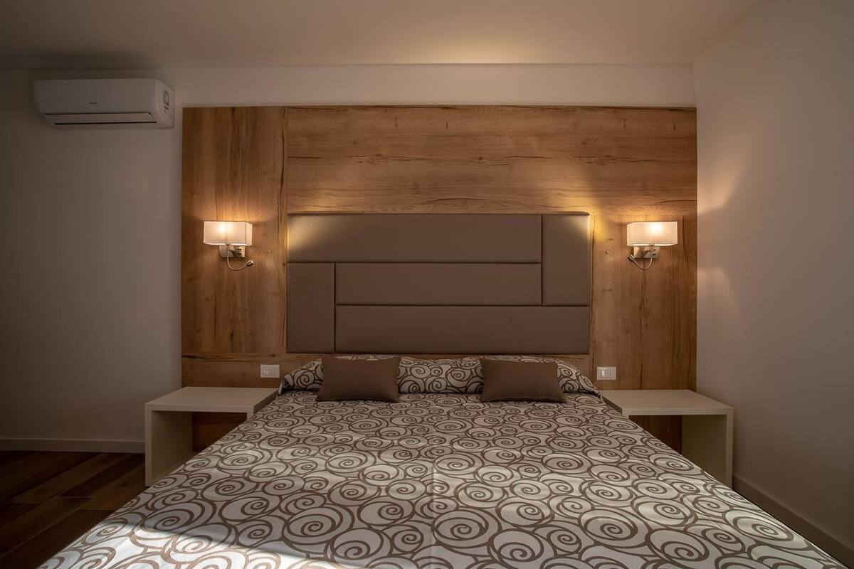 A bedroom with a wooden headboard, two bedside tables, and a patterned bedspread.