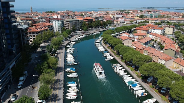 A marina with boats docked along a curved waterfront, surrounded by residential buildings with red-tiled roofs. - Aparthotel Miramare (Grado)