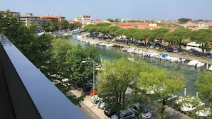 A riverside view with boats docked, trees lining the path, and buildings in the background. - Aparthotel Miramare (Grado)